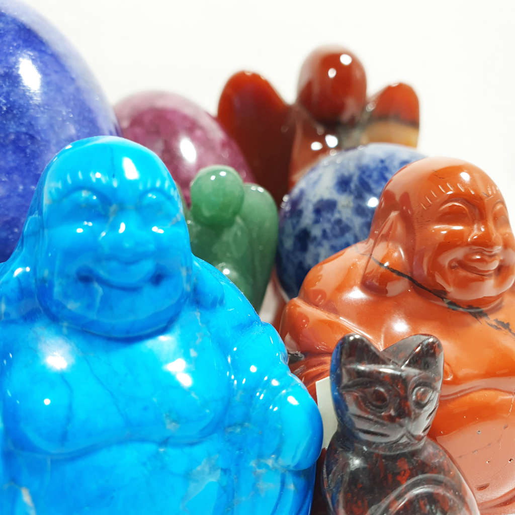 A selection of brightly coloured carved crystal buddhas, cats and angels with a couple of eggs and spheres in the background