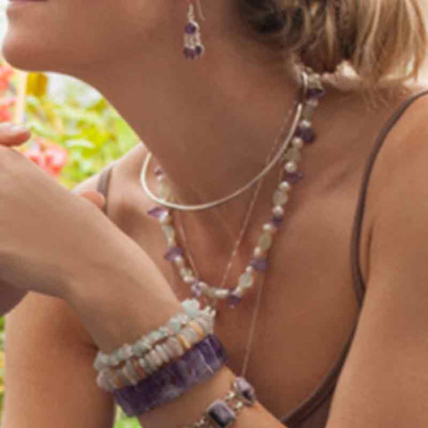 Close up of lady wearing earrings, two crystal necklaces and a variety of bracelets also made from natural crystal