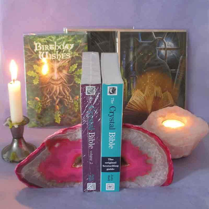 Two crystal bibles held between a pair of pink agate geode bookends, with greeting cards in the background and a candle, and a tealight holder made from a chunk of rose quartz to the side.